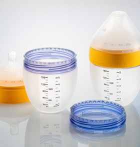 Two baby bottles and their parts on a reflective surface. One bottle is fully assembled with a yellow ring; the other is disassembled, showing a milk-filled container beside its purple and blue rings.