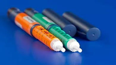 Two uncapped insulin pens, one orange and one green, lie on a blue surface with their dark blue caps behind them.
