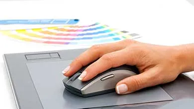 Female hand on computer mouse, grey mousepad, colorful swatch guide in background.