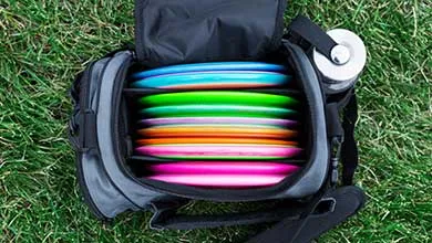 Open black disc golf bag on grass, filled with colorful discs and a water bottle in the side pocket.