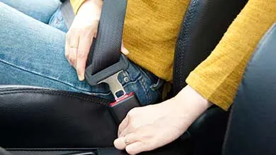 A person in a yellow sweater and blue jeans fastens their seatbelt in a car.