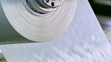 Close-up of an industrial machine unwinding a spool of thin white material.