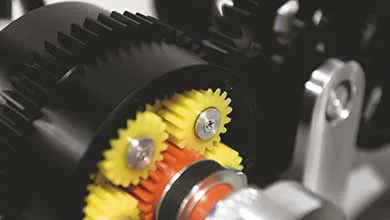 Close-up of a mechanical assembly with small yellow and orange gears meshed with a larger black gear.