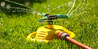 Watering a green lawn in the garden. Garden hose and sprayer. Splashes of water in the sun